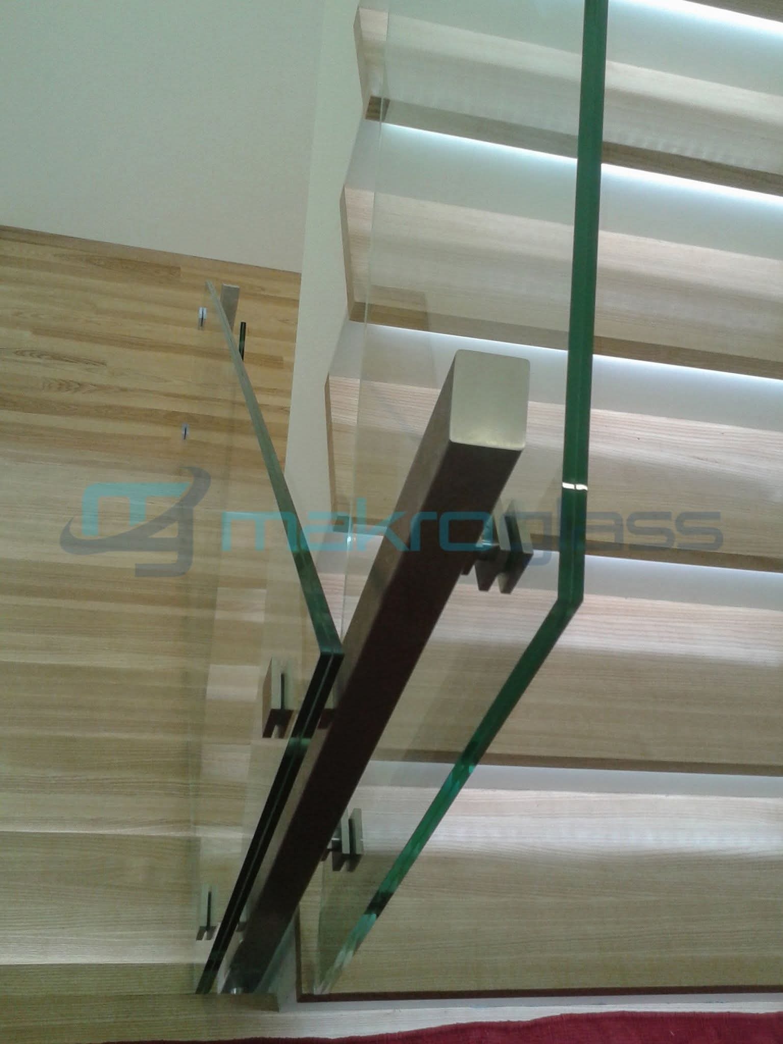 Szklana balustrada schodowa z drewnianymi elementami montowana do ściany z drewnianą okładziną, widok z góry, nowoczesny design.