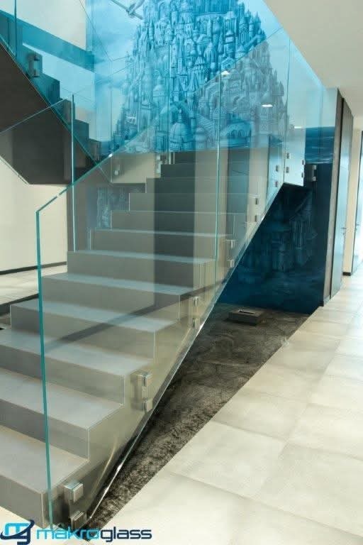 Nowoczesne schody z szklaną balustradą, ozdobione artystycznym malowidłem na ścianie, tworzące unikalny efekt wizualny. Minimalistyczny design i dbałość o detale.