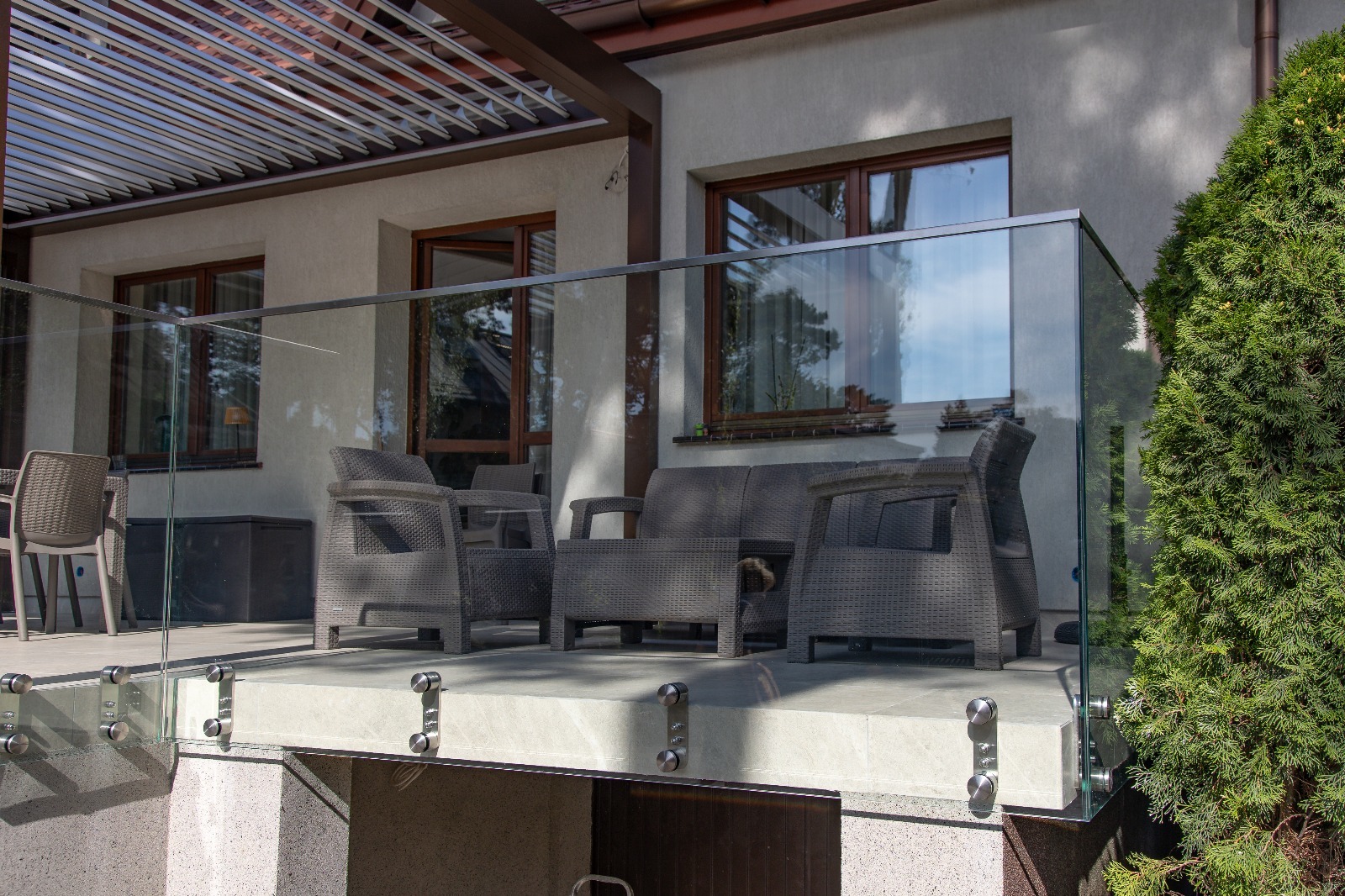 Szklana balustrada balkonu z meblami ogrodowymi i widokiem na budynek z brązowymi oknami. Elementy mocujące ze stali nierdzewnej. Nowoczesny design.