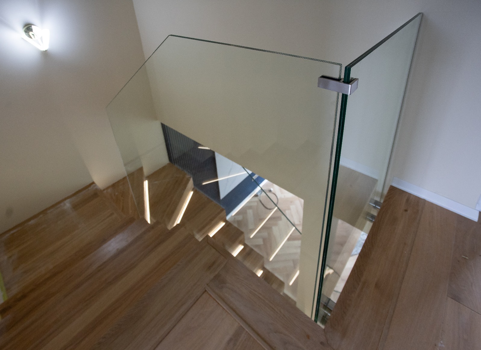 Szklana balustrada na schodach z drewnianymi stopniami, widok z góry. Minimalistyczny design, oświetlenie LED na stopniach. Metalowe mocowania szkła.