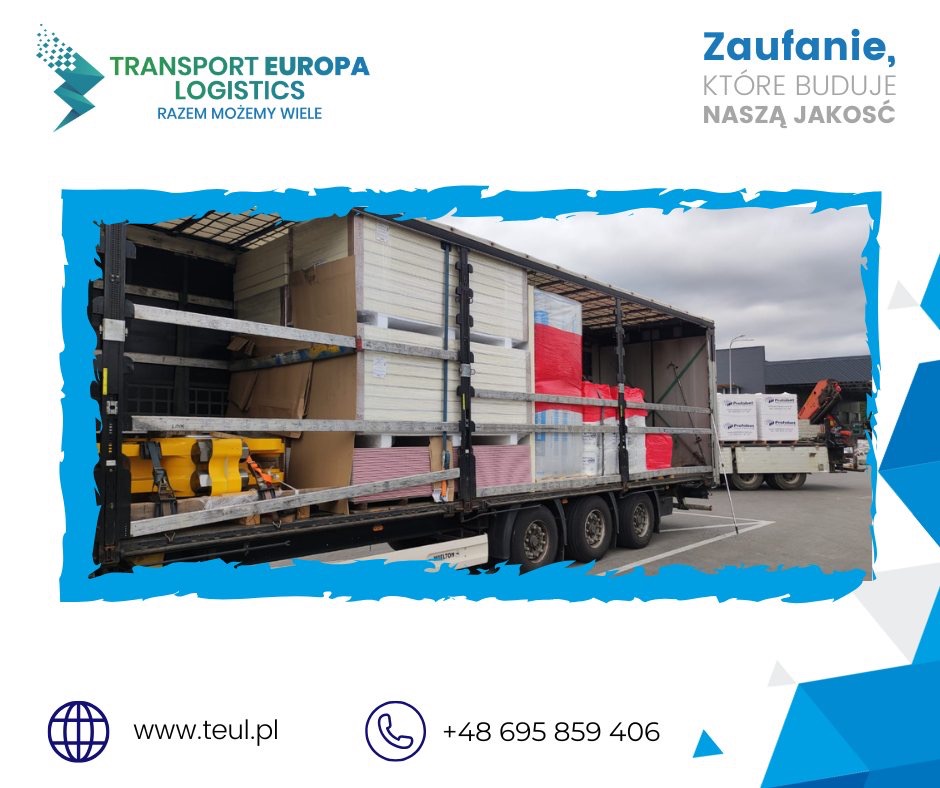 Ciężarówka z otwartą naczepą załadowana materiałami budowlanymi, zabezpieczonymi pasami. Widoczny budynek w tle, logo firmy transportowej.