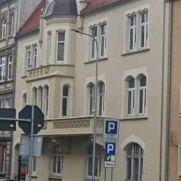 Kancelaria Adwokacka Adwokat Arkadiusz Malak Sprawy rodzinne o rozwód alimenty kontakty Sprawy majątkowe Nieruchomości Sprawy karne - Kamienica w stylu secesyjnym z wykuszem i balkonem, widoczna z ulicy z zaparkowanymi samochodami i znakami drogowymi. Budynek z czerwoną dachówką.