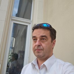 Kancelaria Adwokacka Adwokat Arkadiusz Malak Sprawy rodzinne o rozwód alimenty kontakty Sprawy majątkowe Nieruchomości Sprawy karne - Portret mężczyzny w białej koszuli na tle budynku z oknem łukowym, w którym odbija się wnętrze. Okulary przeciwsłoneczne na głowie. Ujęcie z dołu.