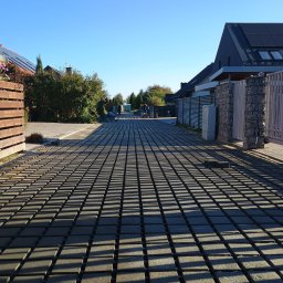Slawomir Gardjas - Długa, wybrukowana kostką droga dojazdowa do domów jednorodzinnych w słoneczny dzień. Widoczni pracownicy w oddali. Geometryczny wzór cieni na kostce.
