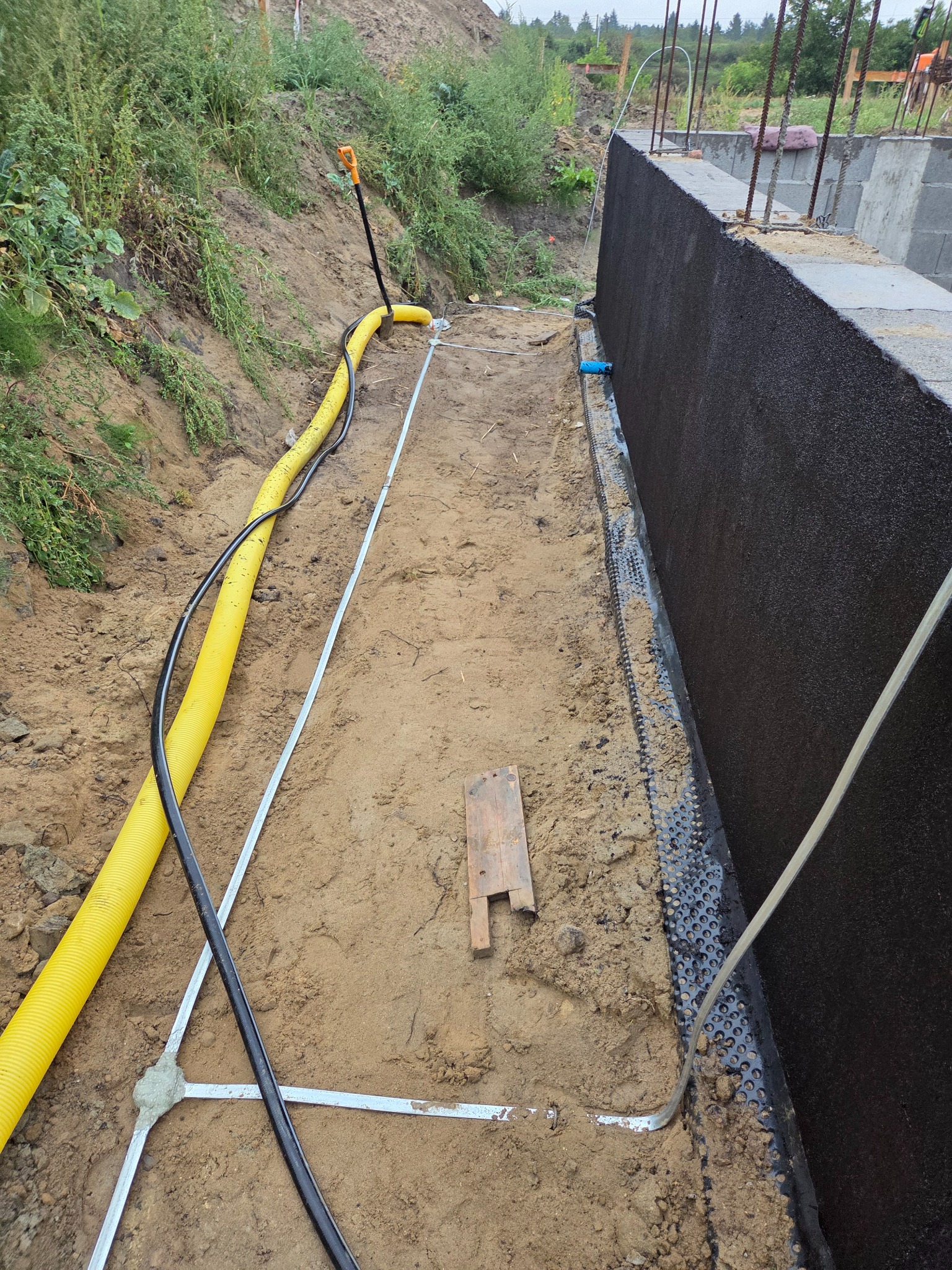 Fundament zabezpieczony hydroizolacją i drenażem w Pelplinie. Żółta rura gazowa w wykopie. Etap prac instalacyjnych przed zasypaniem.