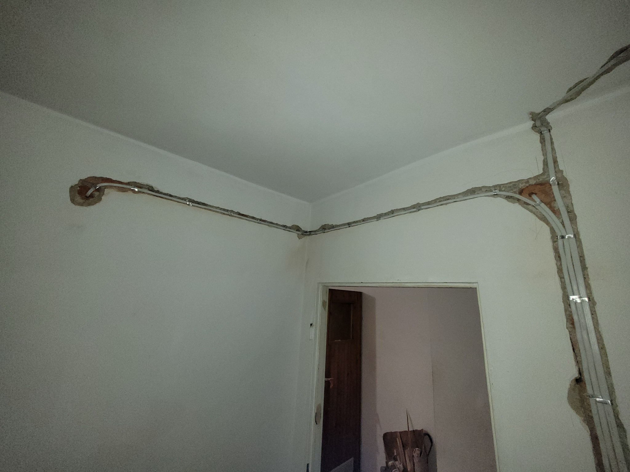 Instalacja elektryczna w bruzdach ściennych, zabezpieczona metalowymi listwami. Widoczne przewody i otwarta przestrzeń, sugerująca remont.