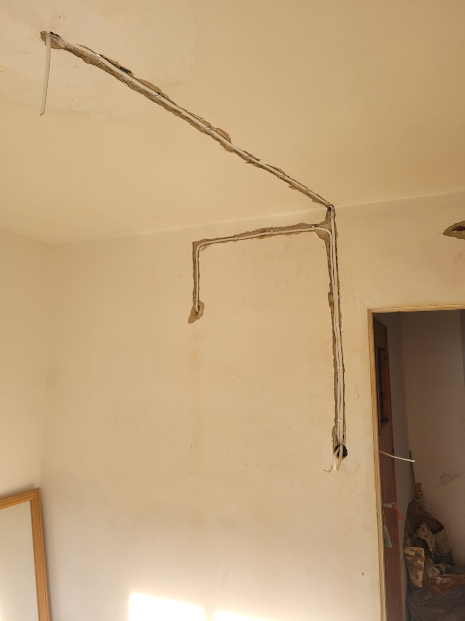 Bruzdowanie ścian pod instalację elektryczną w jasnym pomieszczeniu. Widoczne przewody w wyżłobionych kanałach, przygotowane do dalszych prac wykończeniowych.