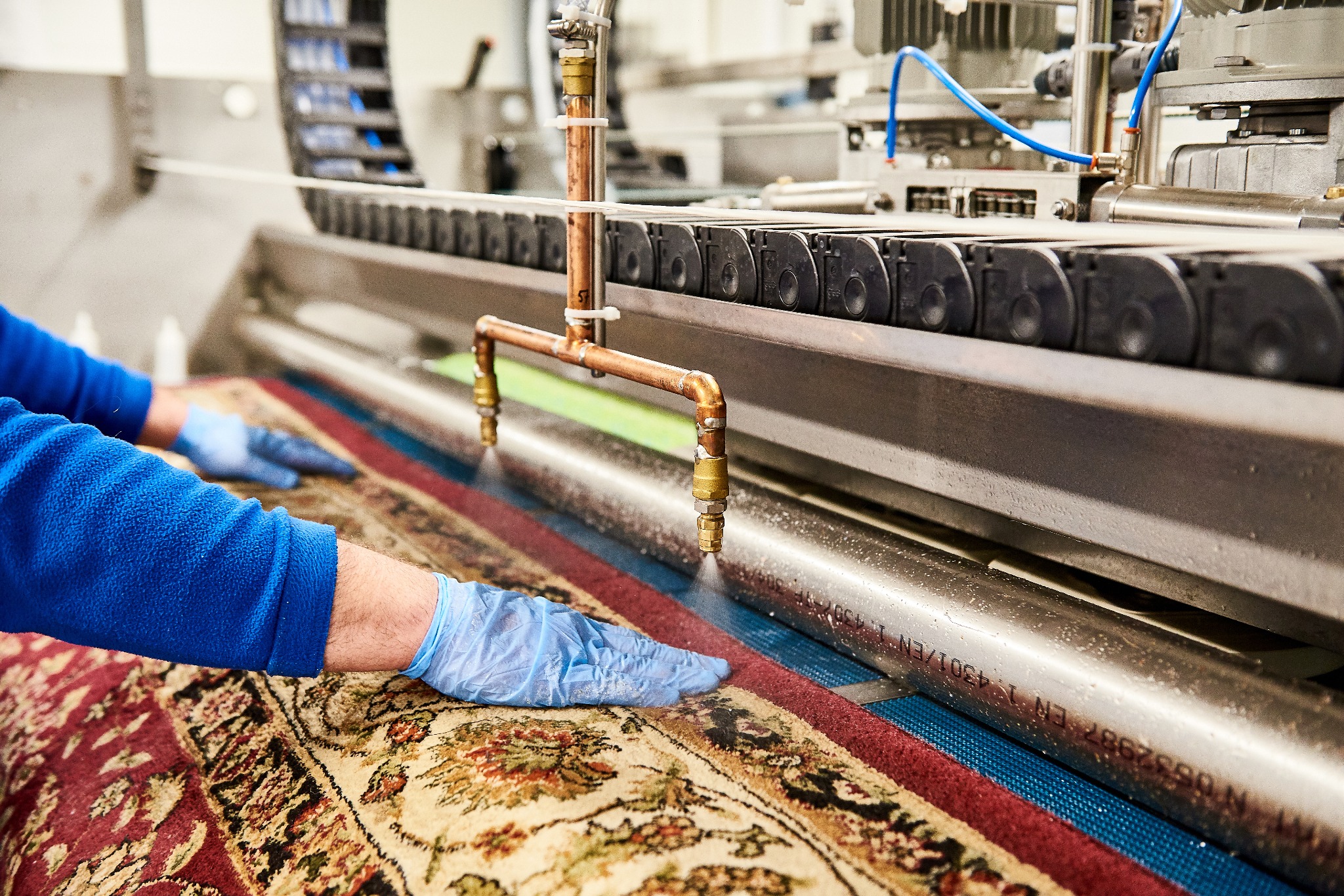 Profesjonalne pranie dywanu orientalnego z użyciem specjalistycznej maszyny z dyszami i niebieskim podkładem, obsługiwane przez osobę w niebieskich rękawiczkach.