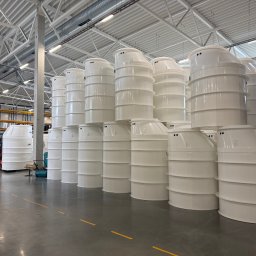 Zakład rzemieślniczy Popa & Kwiatkowski - Magazyn pełen białych, plastikowych zbiorników na szambo lub oczyszczalnie ścieków, ustawionych w rzędach. W tle widoczny wózek widłowy i regały.