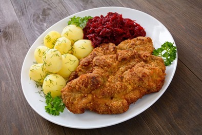 Apetyczny zestaw obiadowy na białym talerzu: panierowany kotlet, gotowane ziemniaki z koperkiem i czerwona kapusta na drewnianym stole.