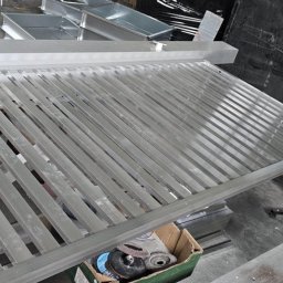 Mateusz Groszek - Metalowa konstrukcja balustrady z profili, widoczne narzędzia i elementy montażowe w tle. Szlifowany metal w surowym stanie, przygotowany do dalszej obróbki.