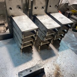 Mateusz Groszek - Metalowe elementy konstrukcyjne po spawaniu, widoczne spoiny, otwory montażowe. Praca ślusarska z Wołomina, detale z bliska, surowy metal, warsztatowy charakter.