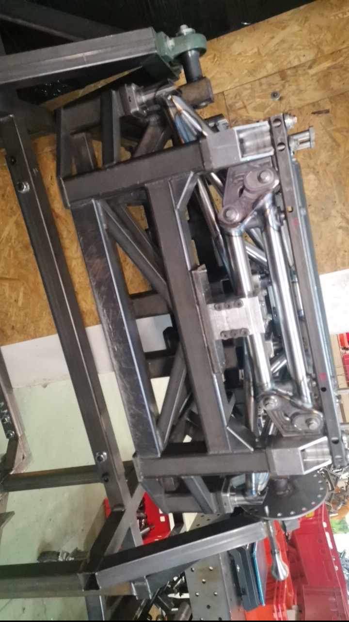 Konstrukcja metalowa z profili i rur, spawana, widoczne elementy mechaniczne, prawdopodobnie w trakcie budowy lub testowania, w warsztacie.