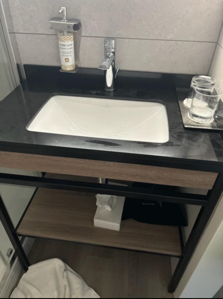 Nowoczesna umywalka nablatowa w łazience z czarnym blatem i metalową ramą, uzupełniona o dozownik mydła i szklanki, tworząca minimalistyczny design.