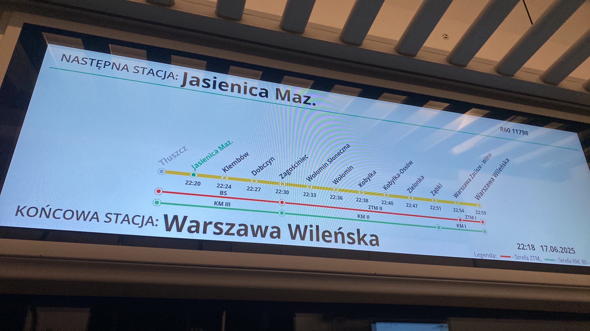 Ekran w pojeździe komunikacji miejskiej prezentujący trasę przejazdu z zaznaczonymi stacjami i godzinami przyjazdu. Widoczne nazwy stacji: Jasienica Maz., Warszawa Wileńska.