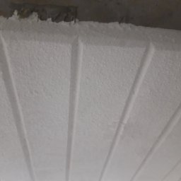 MAR-BUD - Biała, świeżo położona gładź na suficie z widocznymi, równoległymi liniami. Tekstura gładzi jest delikatnie chropowata, a linie tworzą subtelny wzór.