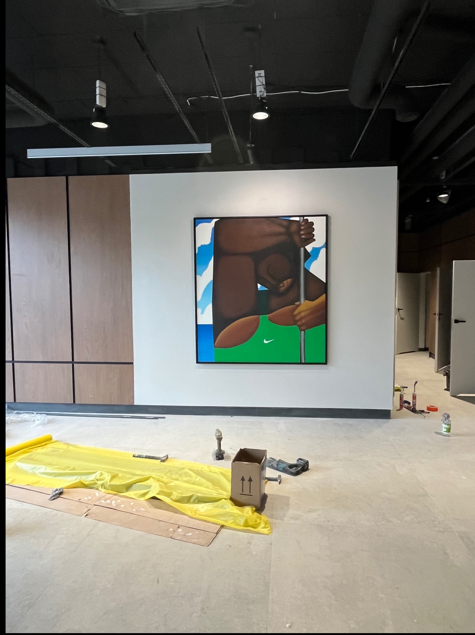 Wnętrze w trakcie prac wykończeniowych: zabezpieczona podłoga folią, narzędzia, obraz na ścianie. Widoczne elementy instalacji pod sufitem i drzwi do pomieszczeń.