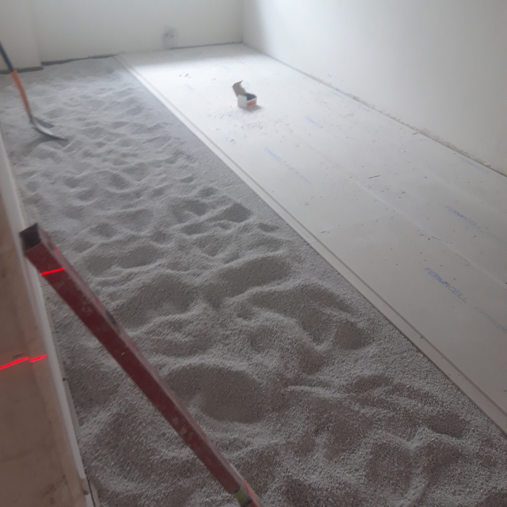 Wyrównywanie podłoża pod panele podłogowe za pomocą granulatu. Widoczny poziomica laserowa i płyty Fermacell. Przygotowanie do układania paneli w jasnym pomieszczeniu.