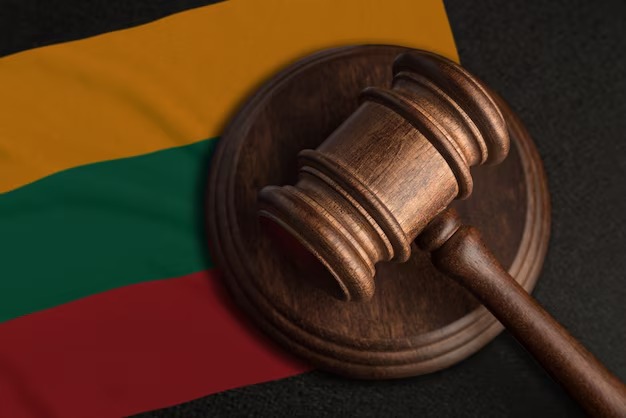 Drewniany młotek sędziowski na tle flagi Litwy, symbol sprawiedliwości i prawa w kontekście litewskiego systemu prawnego. Detaliczne ujęcie.