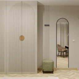 Beżowa szafa z ryflowanymi drzwiami i okrągłymi uchwytami w nowoczesnym wnętrzu z lustrem w kształcie łuku i drewnianą podłogą.