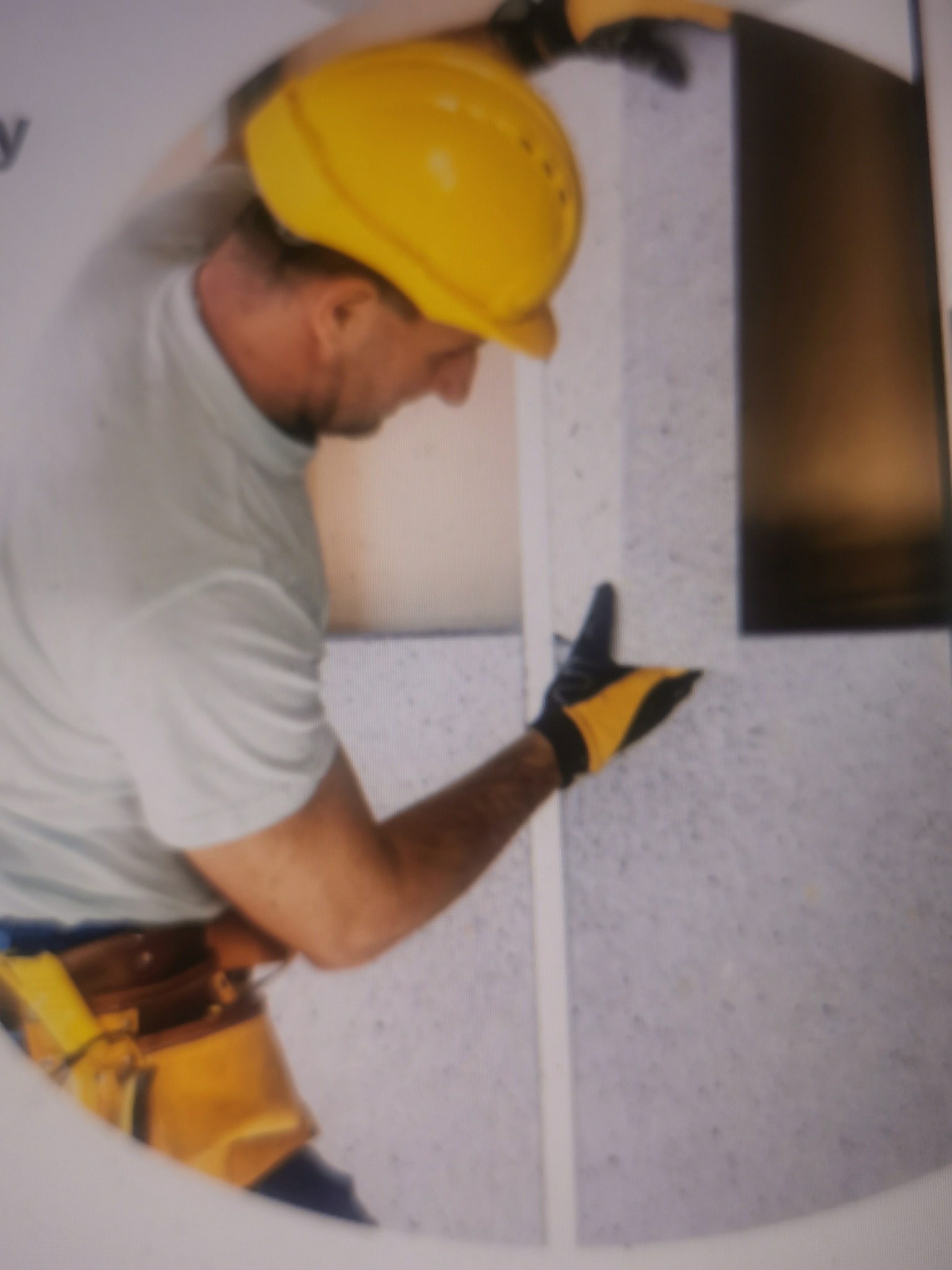 Pracownik w kasku montuje panele akustyczne na ścianie. Widoczne narzędzia i fragment okna. Praca w trakcie realizacji, poprawa akustyki pomieszczenia.