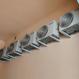 KlimAlex - Pompy ciepła, Klimatyzacja, Ogrzewanie podłogowe - Rząd klimatyzatorów Panasonic zamontowanych na ścianie w jasnym pomieszczeniu. Widoczne wsporniki i detale instalacji. Ujęcie z dołu, podkreślające regularność rozmieszczenia.