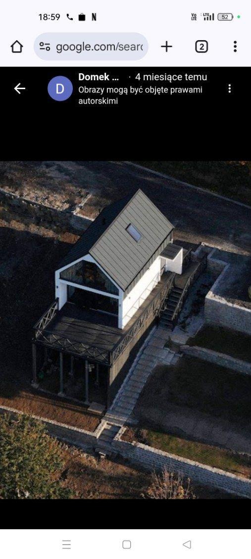 Nowoczesny dom z szarą dachówką, białą elewacją i ciemnym tarasem, widziany z góry. Minimalistyczny design, otoczony surowym krajobrazem.