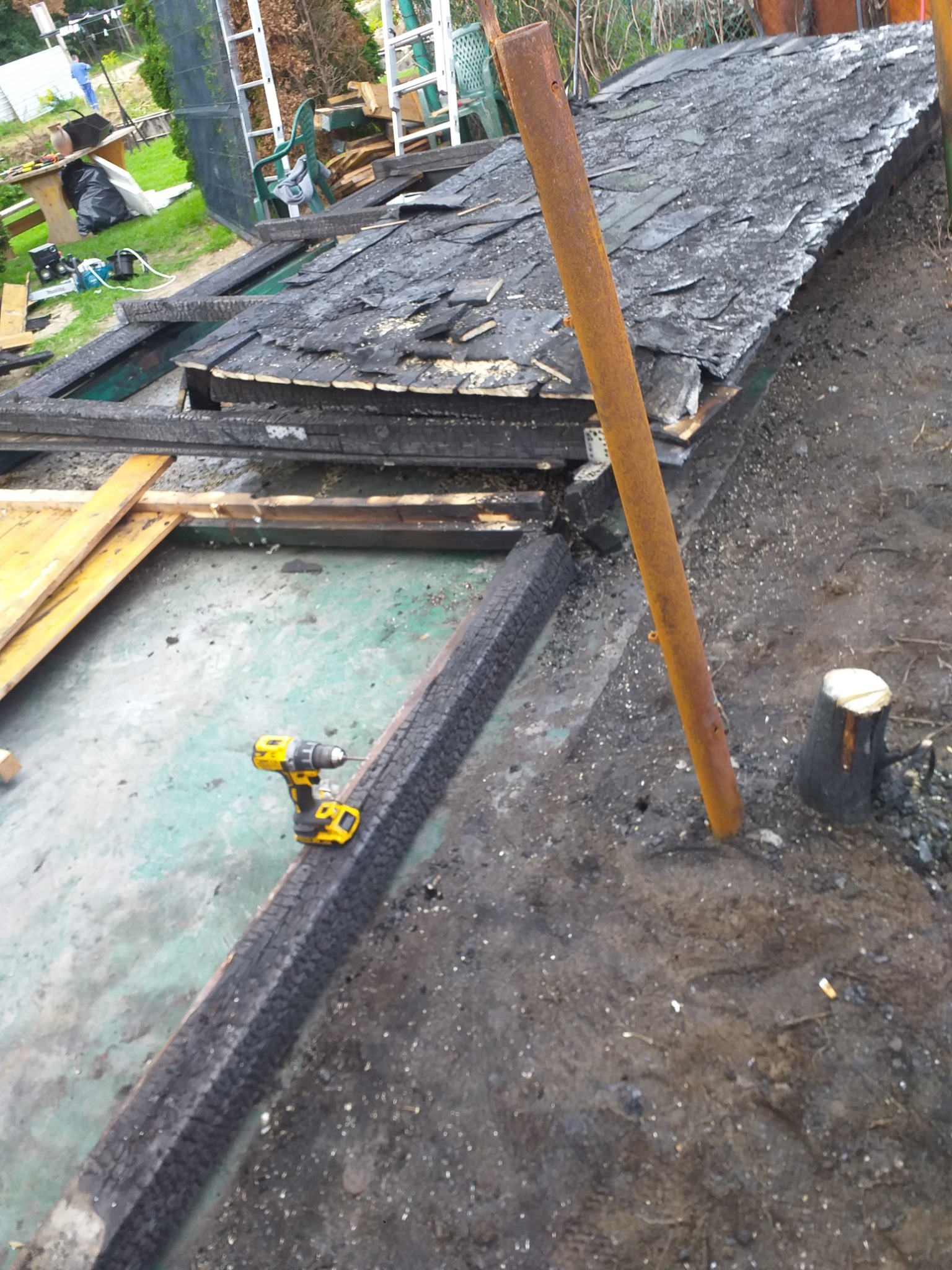 Demontaż zniszczonej konstrukcji dachu z papy. Widoczna wiertarka akumulatorowa, elementy drewniane i metalowe. Prace rozbiórkowe w toku.