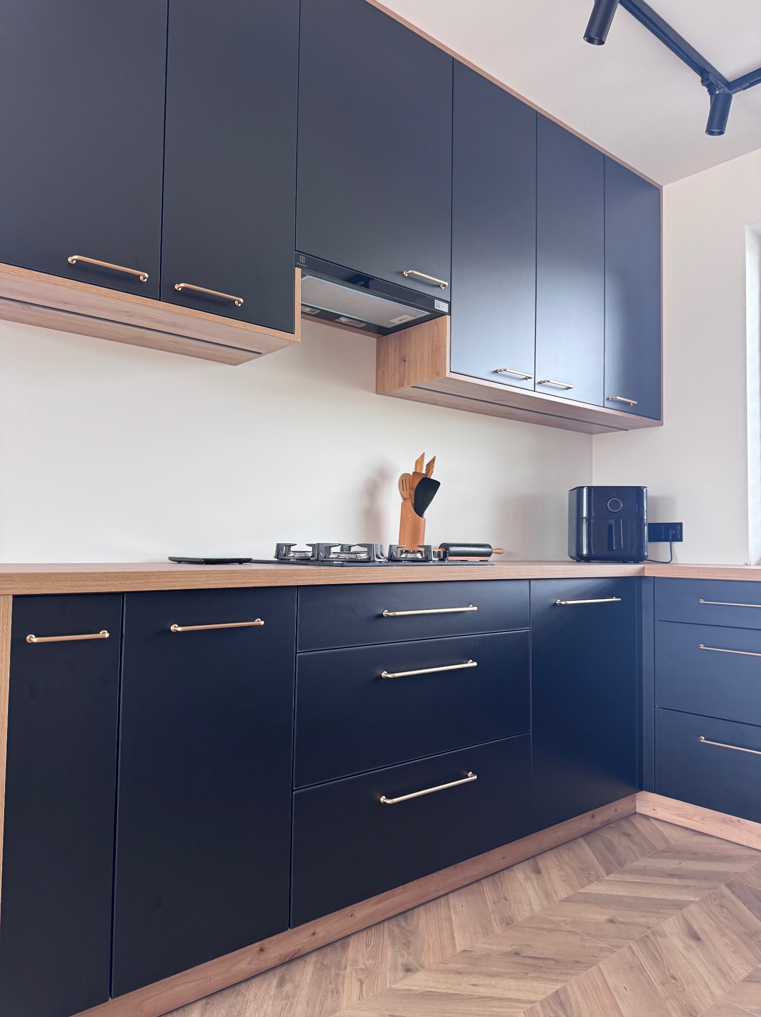 Zabudowa kuchni z płyty laminowanej w kolorze czarnym, blat i zabudowa wysoka w dekorze drewnopodobnym.