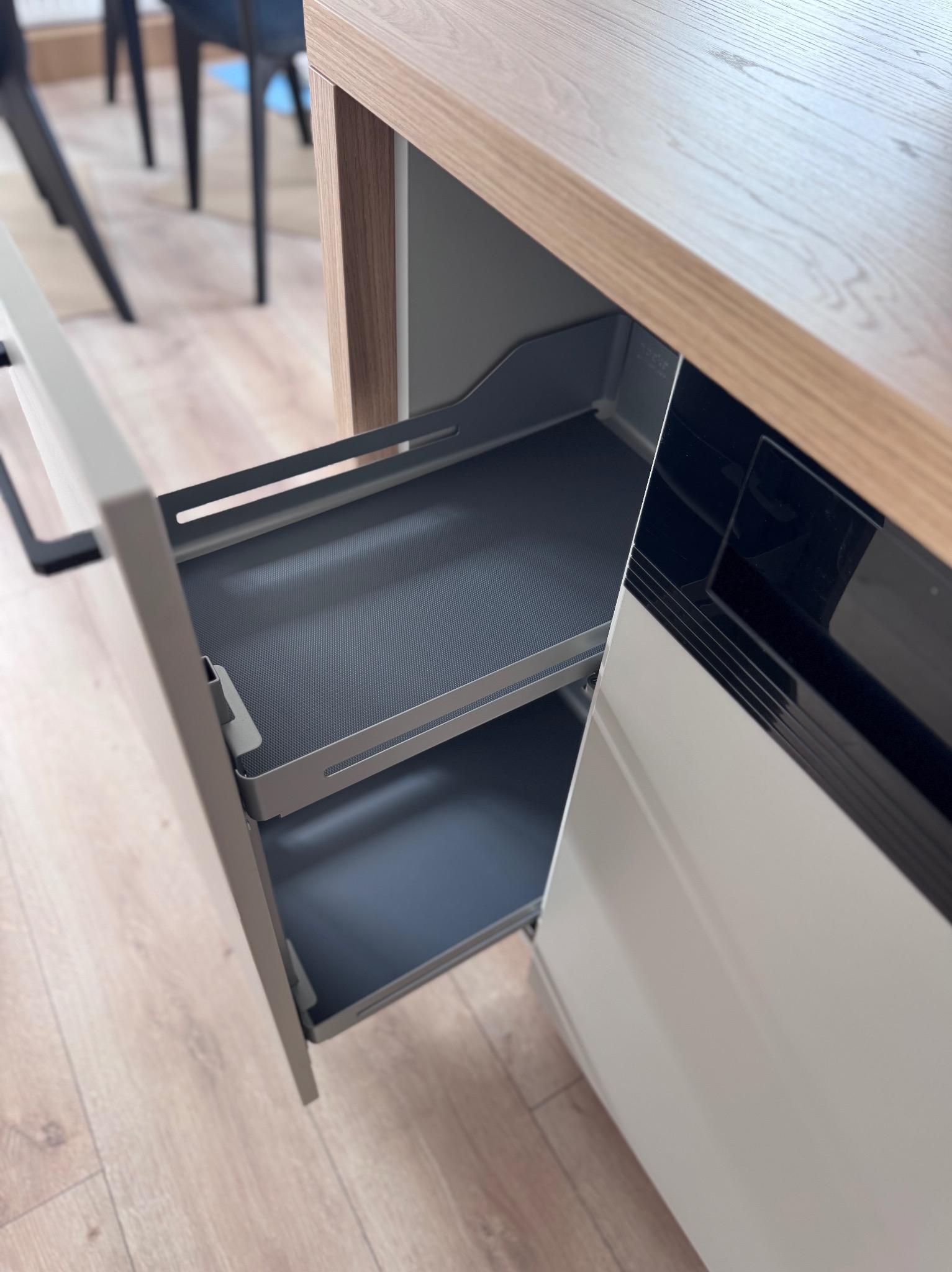 Wysuwana, dwupoziomowa szuflada cargo w nowoczesnej zabudowie kuchennej z blatem imitującym jasne drewno. Widoczna faktura szuflady i mechanizm wysuwu.