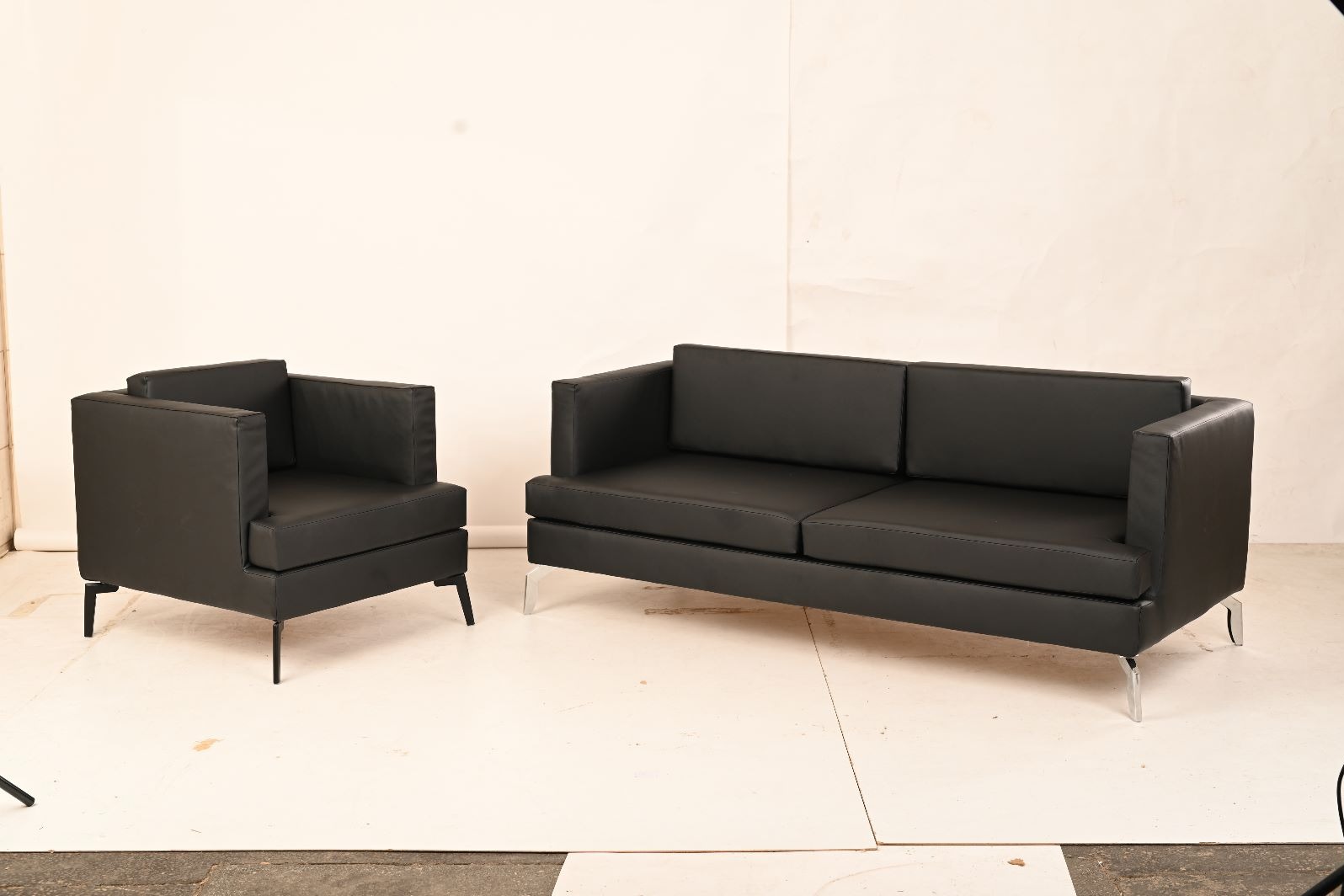 Nowoczesny komplet wypoczynkowy: czarna skórzana sofa dwuosobowa i fotel z metalowymi nóżkami na jasnym tle. Minimalistyczny design, proste linie.