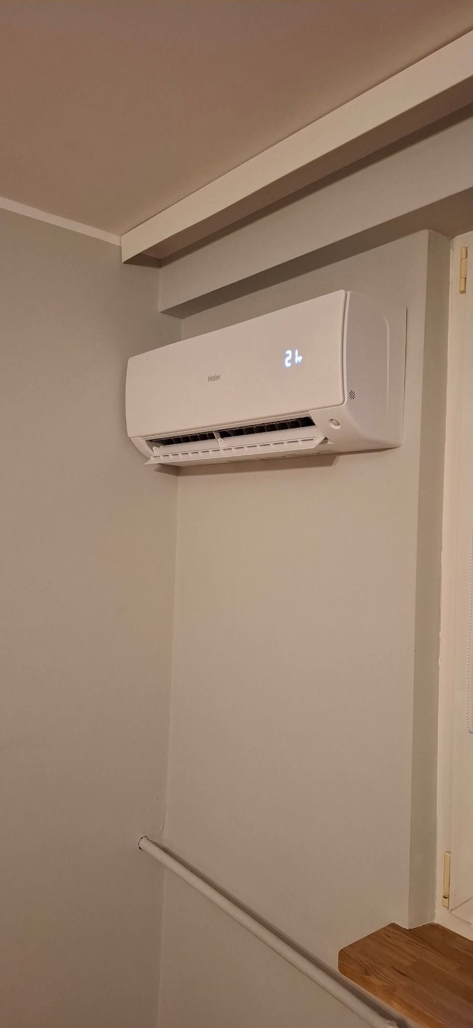 Biała klimatyzacja Haier w jasnym wnętrzu, widoczny wyświetlacz temperatury na 21 stopni, minimalistyczny design, zamontowana na ścianie, neutralne tło.