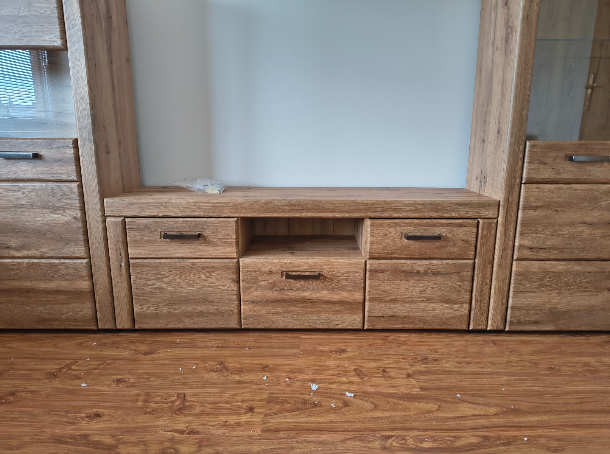 Drewniana meblościanka z szufladami i półkami, po montażu widoczne drobne ślady na podłodze. Ujęcie z bliska, prezentujące strukturę drewna i detale wykończenia.