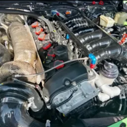 Szczegółowe ujęcie silnika samochodowego po tuningu, z widocznymi elementami układu dolotowego i wtryskowego, osłoną termiczną turbosprężarki i precyzyjnymi połączeniami przewodów.