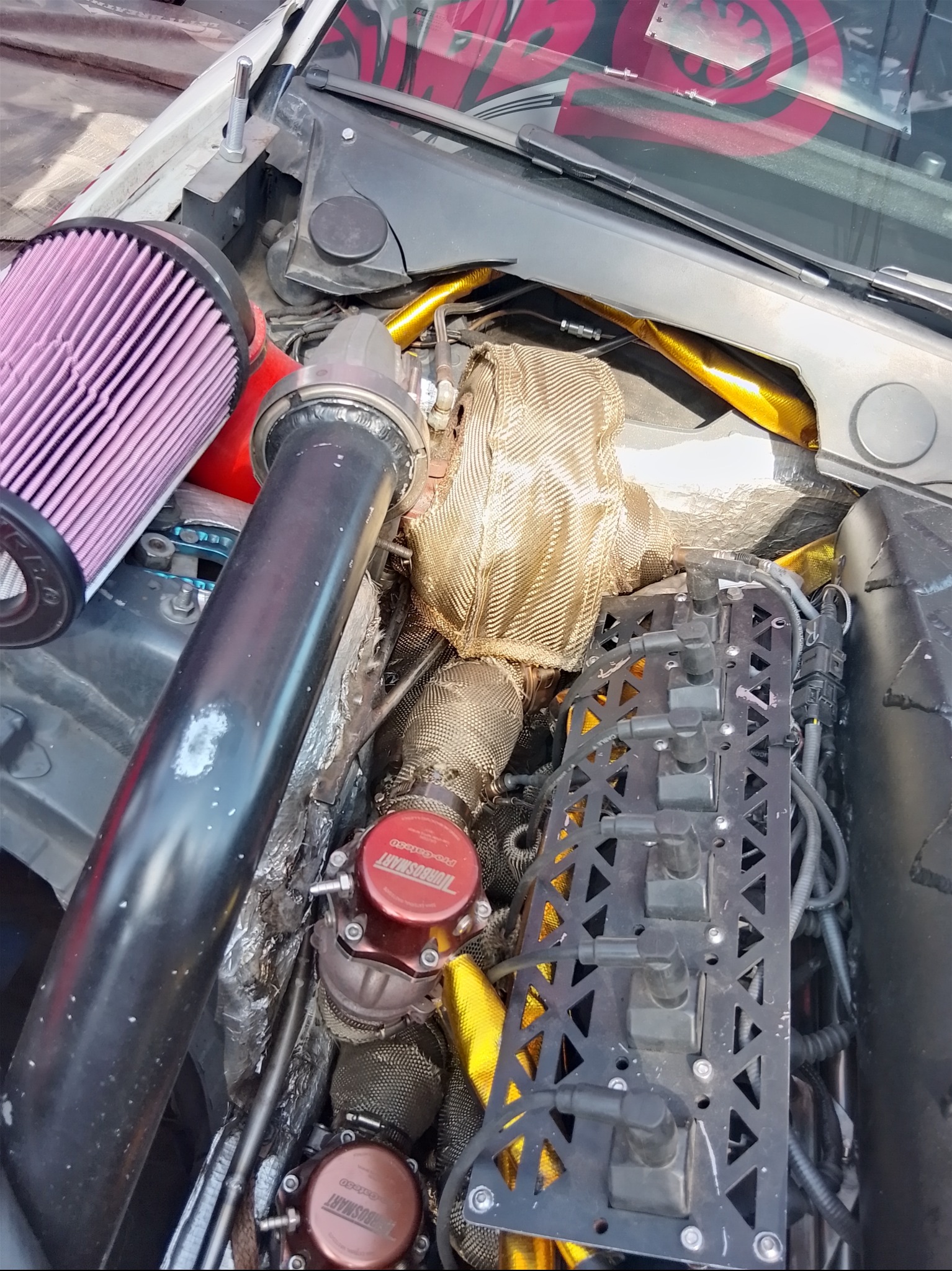 Silnik samochodu po tuningu, z widocznym filtrem powietrza w kolorze fioletowym, osłoną termiczną na turbosprężarce i elementami układu dolotowego powietrza.