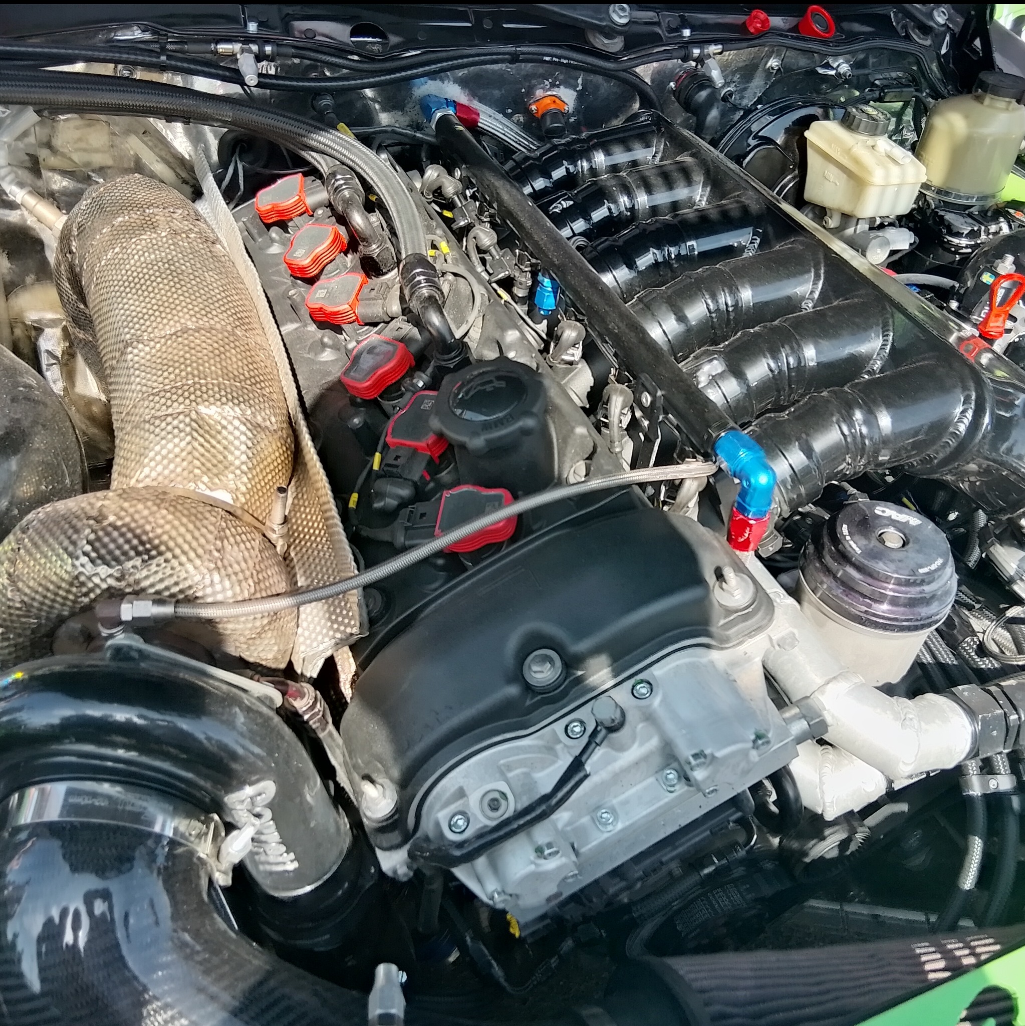 Szczegółowe ujęcie silnika samochodowego po tuningu, z widocznymi elementami układu dolotowego i wtryskowego, osłoną termiczną turbosprężarki i precyzyjnymi połączeniami przewodów.