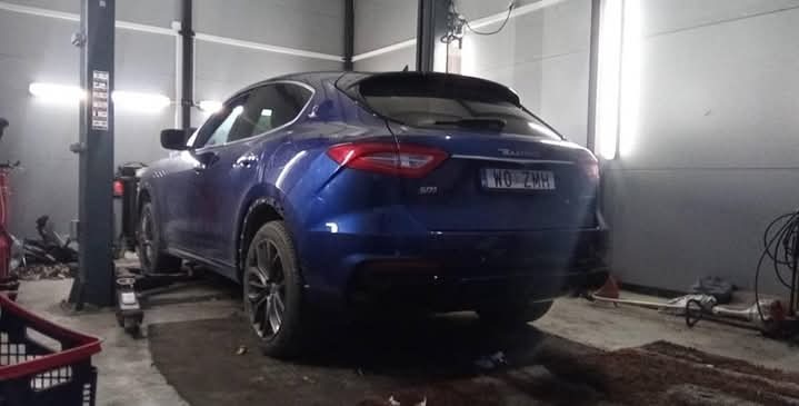 Niebieski Maserati Levante na podnośniku w warsztacie. Widoczny numer rejestracyjny i oświetlenie warsztatowe. Auto ustawione tyłem do widza.
