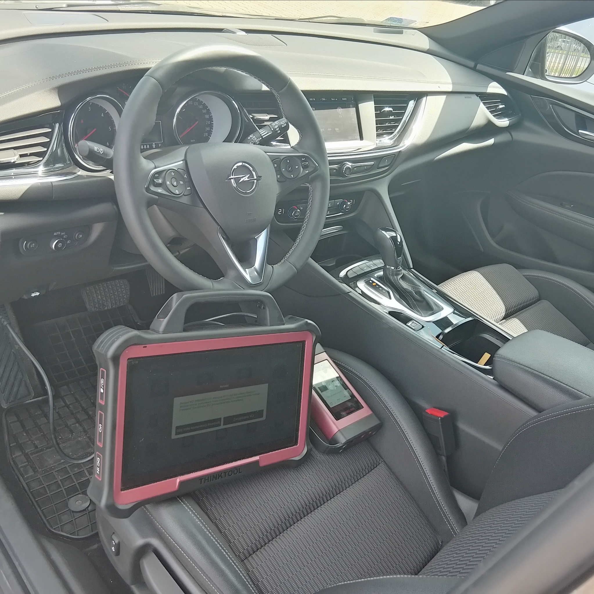 Wnętrze Opla Insignia z urządzeniami diagnostycznymi Thinktool na siedzeniu pasażera, widok na deskę rozdzielczą i kierownicę. Diagnostyka samochodowa.