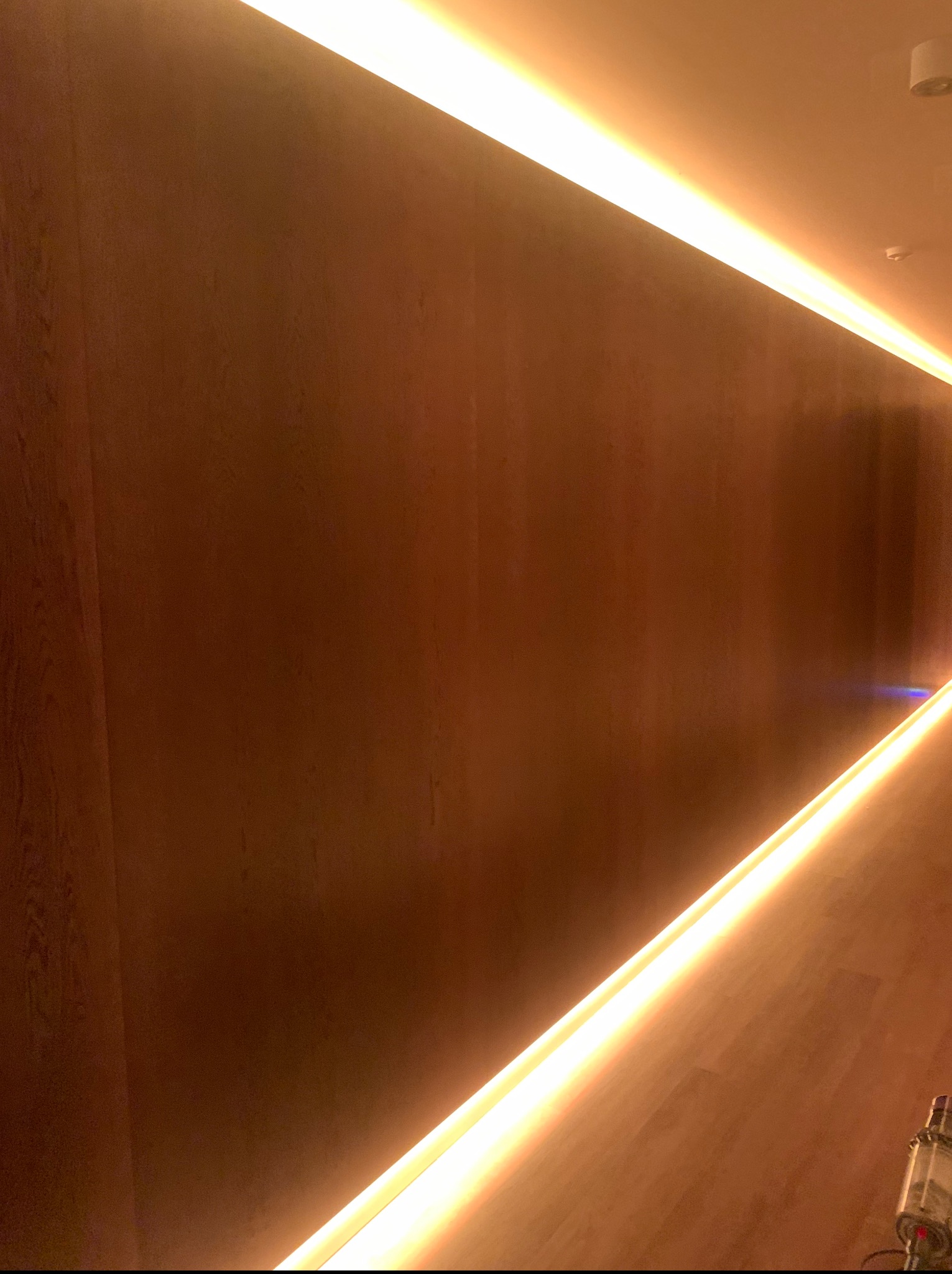 Drewniana ściana z podświetleniem LED wzdłuż górnej i dolnej krawędzi, tworząc efektowny wystrój wnętrza. Ciepłe światło podkreśla strukturę drewna.