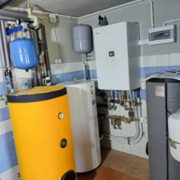 Kompleksowa instalacja grzewcza z zbiornikami w różnych kolorach (żółty, biały, niebieski) i kotłem Nibe SHB 20,  w kotłowni z wykończeniem w płytkach.