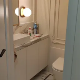 Elegancka łazienka w kremowych tonacjach: marmurowy blat, białe szafki pod umywalką, designerskie oświetlenie i marmurowe płytki podłogowe z czarną obwódką.