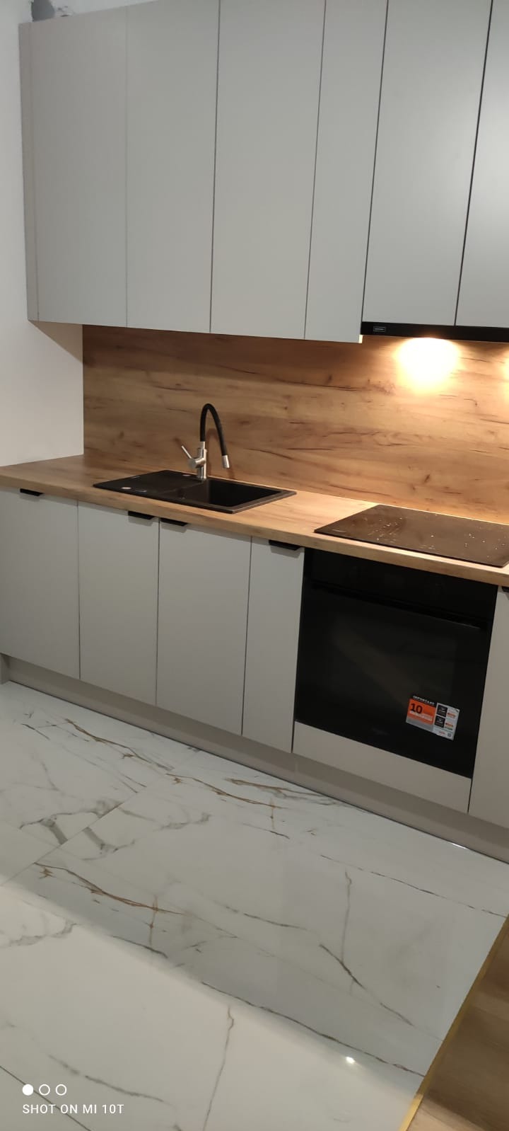 Jasna kuchnia z drewnianym blatem i marmurową podłogą. Nowoczesne szafki bez uchwytów, czarny zlew i płyta indukcyjna. Oświetlenie LED pod szafkami.