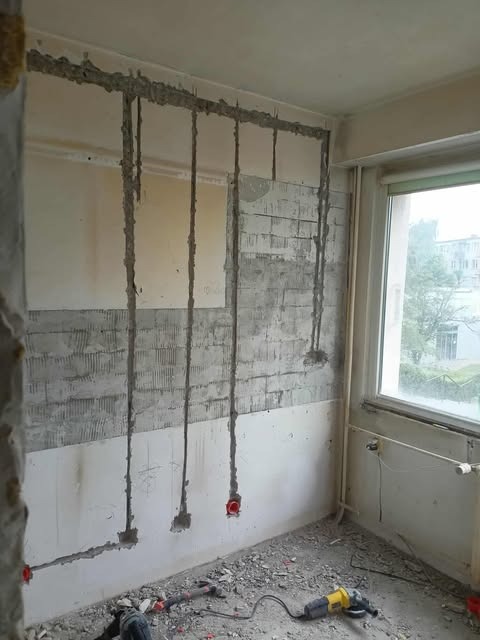 Wewnętrzny remont: wyżłobione bruzdy w ścianie pod instalację elektryczną z widocznymi puszkami, gruzem na podłodze i narzędziami.