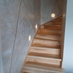 Usługi Wykończeniowe - Drewniane schody z oświetleniem punktowym na ścianie o dekoracyjnej fakturze i geometrycznych liniach. Widoczne włączniki światła.