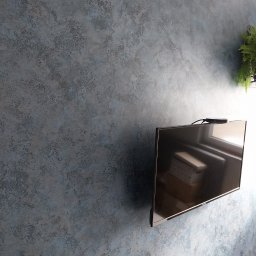 Usługi Wykończeniowe - Ściana z dekoracyjnym, niebiesko-szarym tynkiem strukturalnym, obok wiszący telewizor i roślina doniczkowa. Widoczne niedoskonałości i nierówności faktury.