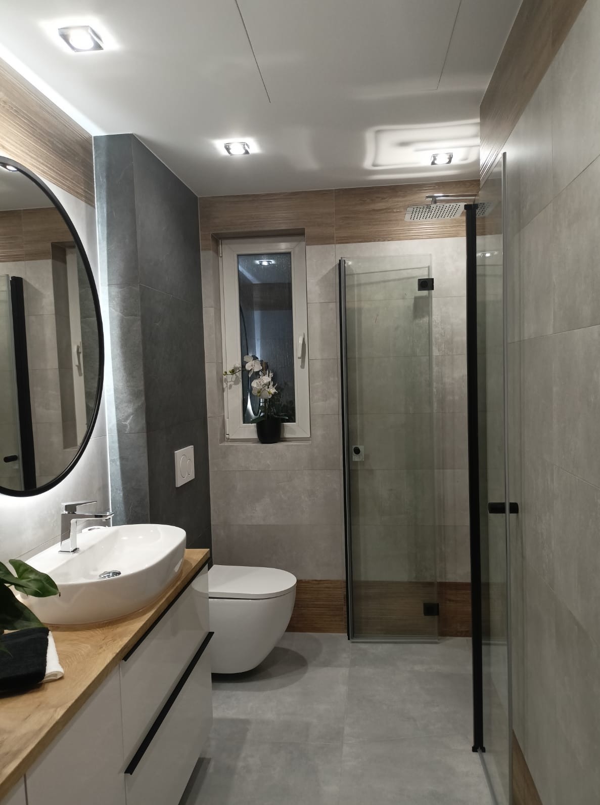 Nowoczesna łazienka po remoncie w Strzelcach Opolskich. Umywalka nablatowa, lustro w czarnej ramie, kabina prysznicowa z czarnymi profilami i szara glazura.