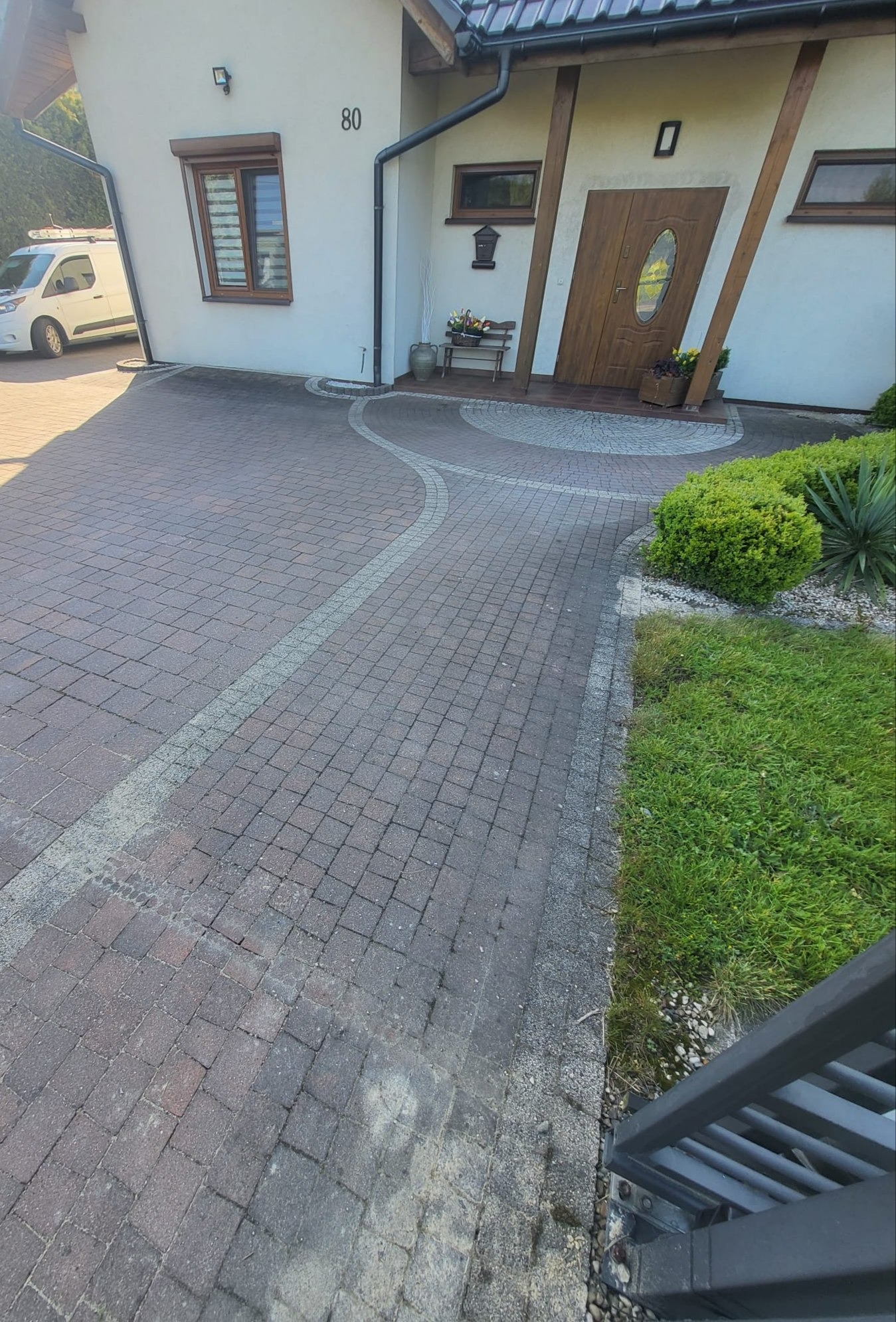 Czerwona kostka brukowa przed domem z numerem 80, z widocznymi śladami zabrudzeń i mchu, sugerująca potrzebę czyszczenia. Częściowo widoczny biały van.
