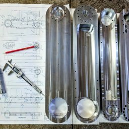 FIL-KAM SPÓŁKA Z OGRANICZONĄ ODPOWIEDZIALNOŚCIĄ - Precyzyjnie obrobione metalowe elementy na rysunku technicznym z ołówkiem i narzędziami pomiarowymi. Widoczne otwory i frezowania.