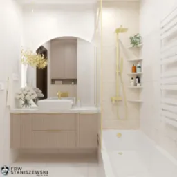 Elegancka łazienka w beżach i bieli z akcentami złota: umywalka nablatowa, bateria, kabina prysznicowa. Uwagę przykuwa lustro w kształcie łuku i dekoracyjny żyrandol.