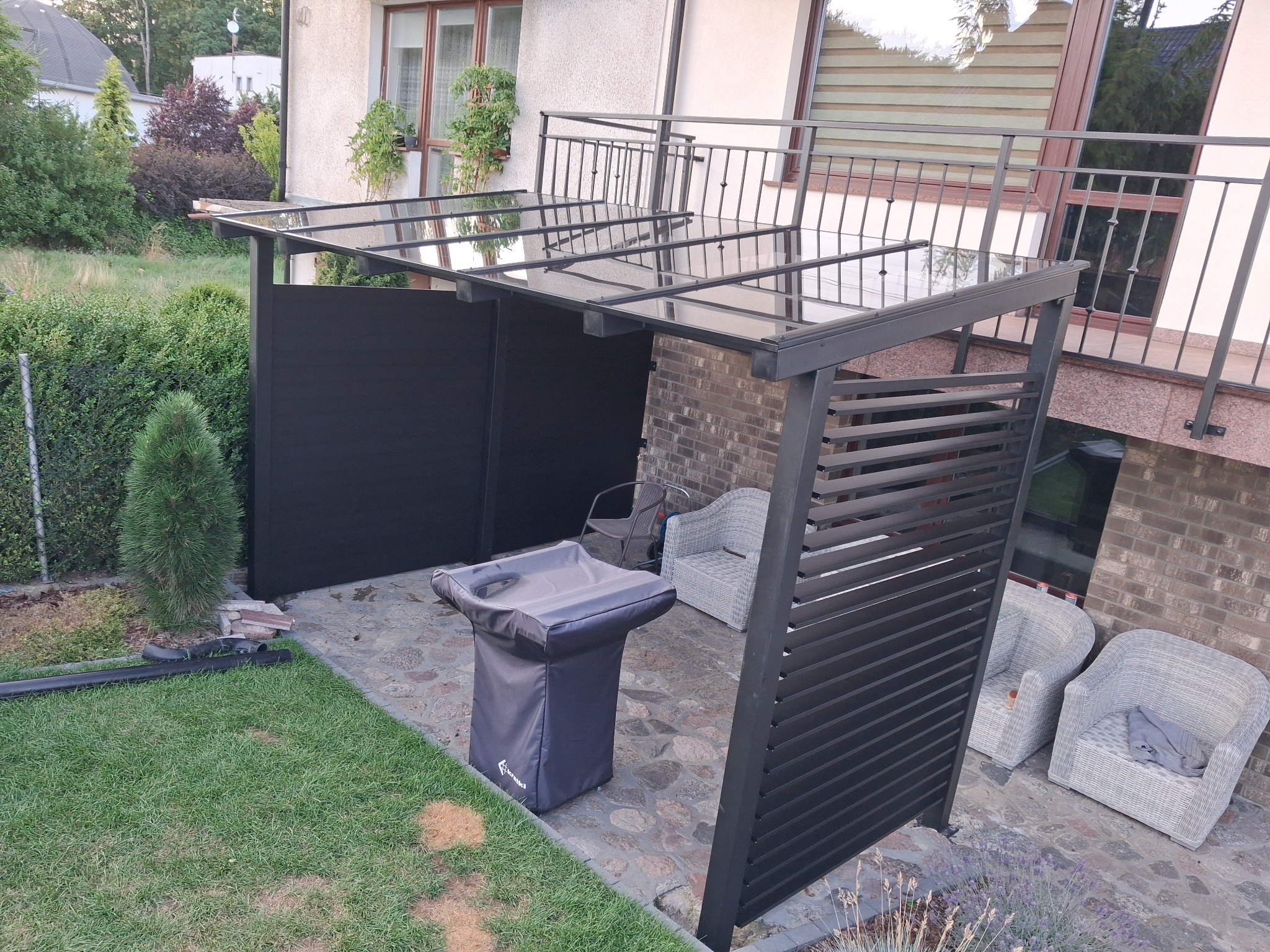 Nowoczesna, metalowa pergola z zadaszeniem w Dzierżążnie, przylegająca do budynku, z elementami ażurowymi i pełnymi, tworząca zaciszną przestrzeń.